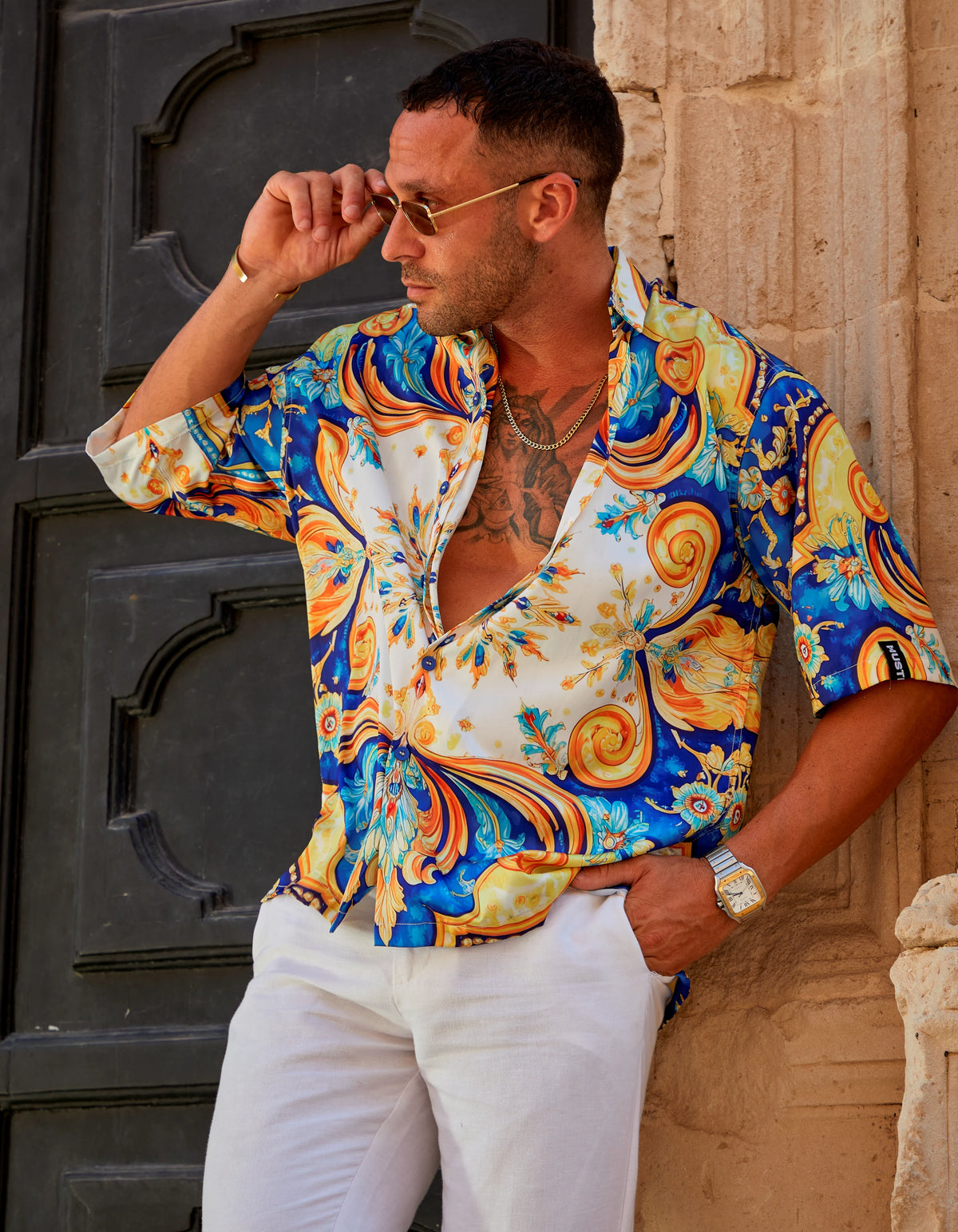 Positano men's satin Cuban collar shirt with white trousers, leaning on a church door, We Hustle