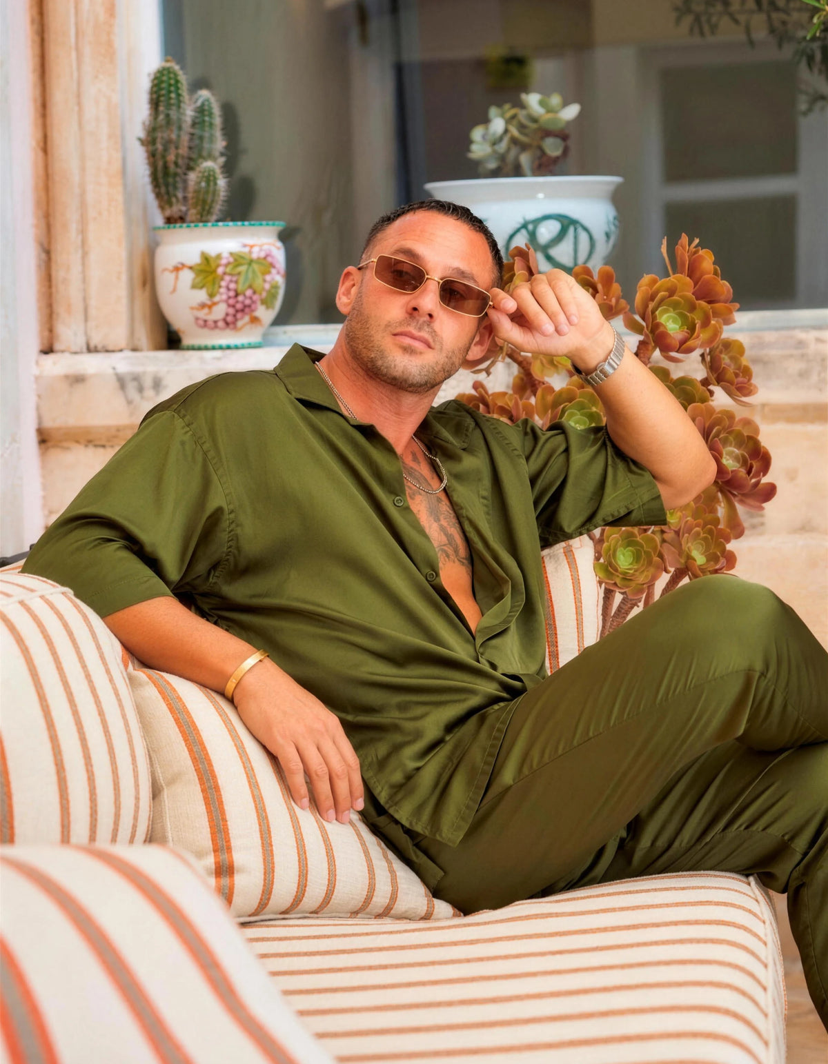 Trouble In Silk men's satin co-ord set, seated on a striped sofa with sunglasses, We Hustle